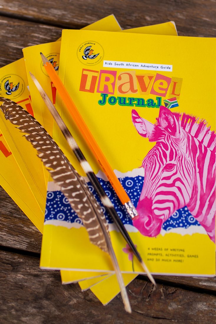 A stack of South African Travel Journals with a pencil and a guinea fowl feather